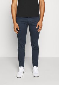 Marineblå slim-fit jeans tillverkade av bomullsmix, med fem fickor och en slät yta, kombinerade med vita sneakers.