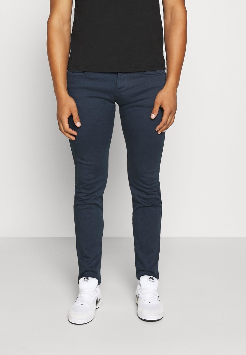 Marineblå slim-fit jeans tillverkade av bomullsmix, med fem fickor och en slät yta, kombinerade med vita sneakers.