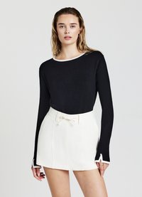 Schwarzes Langarmoberteil mit weißem Besatz am Halsauschnitt und an den Manschetten, kombiniert mit einem weißen, hochgeschnittenen Rock mit Kordelzug und Falten.