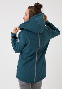 Türkisfarbene Kapuzenjacke aus strukturiertem Stoff, mit seitlichem Reißverschluss und einem Logopatch am Ärmel. Verfügt über einen lässigen Schnitt und eine verstellbare Kapuze.