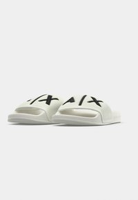 Sandálias brancas tipo slide com parte superior texturizada, com detalhes do logotipo em preto. O design inclui biqueira aberta e uma sola durável.