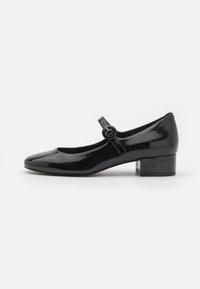 Black patent leather Mary Jane shoe with a round toe, small block heel, and a strap with a circular buckle detail. Smooth, shiny texture.