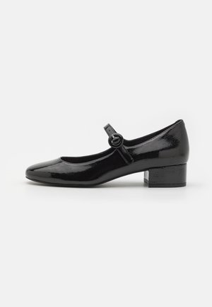 Black patent leather Mary Jane shoe with a round toe, small block heel, and a strap with a circular buckle detail. Smooth, shiny texture.