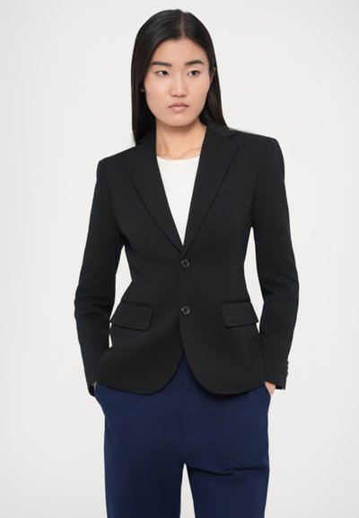 Črn krojen blazer z zarezanimi ovratniki, dvema sprednjima žepoma in dvema gumboma. Oblečen čez belo srajco in modre hlače. Gladek tekstura.