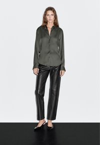 Donkergroen satijnen overhemd met knopen, gecombineerd met zwarte leren broek en zwarte schoenen met een puntige neus, voor een strakke, moderne uitstraling.