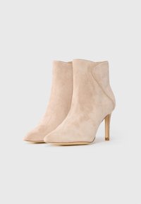 Bottines en suede beige avec un bout pointu, un talon stiletto fin et des détails de panneau latéral subtils, présentant une texture lisse.