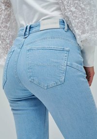 Jeans de mezclilla azul claro con un diseño ajustado, que cuentan con dos bolsillos traseros y una etiqueta de cuero con marca en la cinturilla.