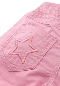 Różowa bawełniana odzież z naszywaną kieszenią. Posiada haftowany wzór w kształcie gwiazdy w nieco ciemniejszym odcieniu różu. Gładka tekstura i prążkowany pas.