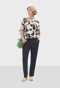 Blůza s námořnickým a krémovým vzorem s 3/4 rukávy, spárovaná s námořnickými kalhotami. Zelená taška a béžové sandály dotvářejí outfit.