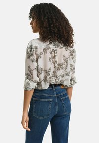 Helle, gemusterte Bluse mit aufgerollten Ärmeln und floralem Design; kombiniert mit dunkelblauen Jeans mit Gesäßtaschen und einem Gürtel.