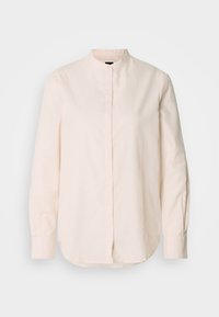 Blouse à manches longues couleur crème avec col montant et boutons cachés sur le devant, présentée sur un fond blanc uni.