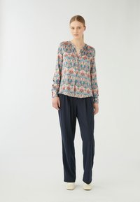 Blusa a maniche lunghe con un motivo floreale colorato nei toni del rosa e dell'azzurro, abbinata a pantaloni a righe navy. Il tessuto ha una consistenza liscia.