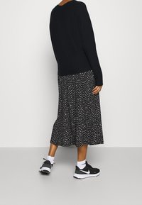 Maglione nero, gonna a fantasia con macchie bianche e sneakers nere. L'outfit combina texture e colori a contrasto.