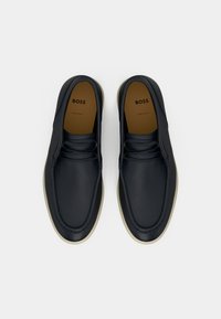 Σκούρα ναυτικά δερμάτινα παπούτσια με λεία υφή, στρογγυλεμένη μύτη και μπεζ λαστιχένια σόλα. Διαθέτουν διακριτικά κορδόνια και ανάγλυφο λογότυπο της μάρκας.