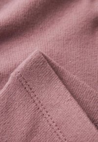 Mauve fabric with a fine ribbed texture, folded to show stitching details. The material appears soft and lightweight.