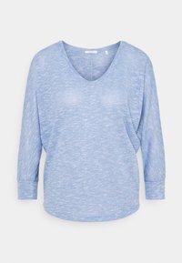 Hellblaues Langarmoberteil mit V-Ausschnitt, lässiger Passform und subtiler Textur. Die Bündchen und der Saum sind leicht gekrümmt für einen lässigen Look.