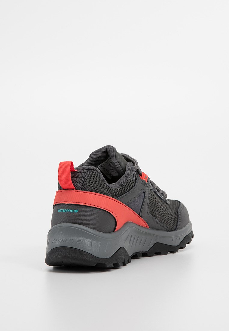 Zapato de senderismo impermeable negro y rojo con suela de grosor elevado, tejido de malla y cuello acolchado, visto desde atrás sobre un fondo blanco.