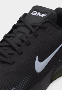 Svart Nike-sneaker med hvitt swoosh-logo, svarte lisser og "air"-merke på den polstrede tungen, med et teksturert prikkmønster på overdelen.