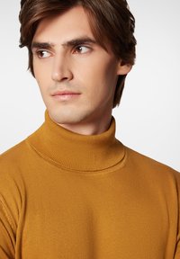 Musztardowa żółta sweter z szerokim kołnierzem, o dopasowanym kroju, lekkiej teksturze i wysokim dekolcie. Zbliżenie na kołnierz i ramiona.