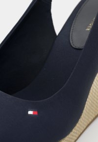 Zapato de cuña azul marino con un tacón de yute texturizado, parte superior de tela suave y un pequeño acento de logo en rojo, blanco y azul cerca del tacón.