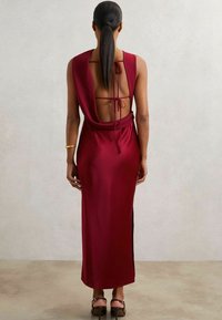 Burgunderfarbenes Satin Kleid mit drapierter offener Rückseite und Bindeschluss, lang und schmal geschnitten sowie seitlichem Schlitz für Bewegungsfreiheit.