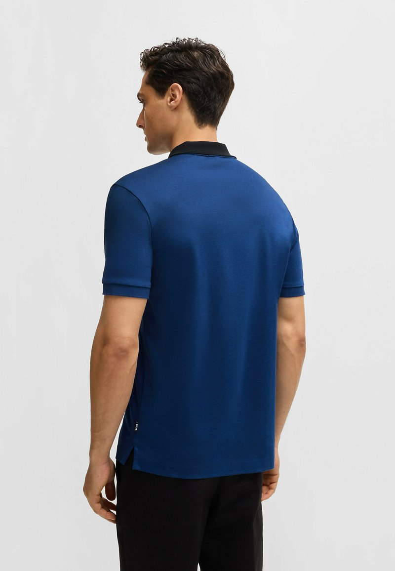 Polo pour homme en bleu marine avec un col noir, à manches courtes, une finition texturée et des fentes sur les côtés à l'ourlet pour un meilleur ajustement.