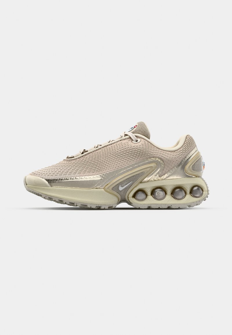Helle beige Sneaker mit einem strukturierten Mesh-Obermaterial, metallischen Akzenten und einem einzigartigen Blasensohlen-Design, das kreisförmige Pods für Dämpfung bietet.
