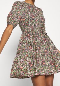 Abito floreale con sfondo nero e fiori multicolori, maniche a sbuffo corte, corpetto aderente e gonna svasata.