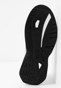 Semelle en caoutchouc noire texturée d'une basket avec des accents blancs et le logo "Versace Jeans Couture" embossé au centre.