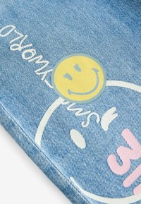 Tissu en denim bleu avec un visage souriant jaune imprimé et un texte blanc et rose avec des formes abstraites.