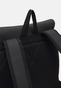 Zaino nero con un pannello in rete texturizzato, schienale imbottito e maniglia superiore per il trasporto. Design elegante con spallacci regolabili e chiusura a rolo.