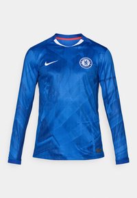 Blå langærmet fodboldtrøje med et geometrisk mønster, Nike-logo og Chelsea FC-emblem. Har en rund hals med røde og hvide detaljer.