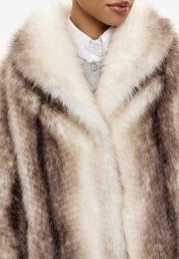 Cappotto in pelliccia sintetica con un ampio e morbido colletto color crema, texture maculata marrone e beige, e una forma leggermente oversize.