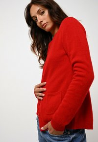 Czerwony kardigan wełniany o miękkiej fakturze, z luźnym krojem, długimi rękawami, guzikami z przodu i dwiema kieszeniami na wysokości talii.