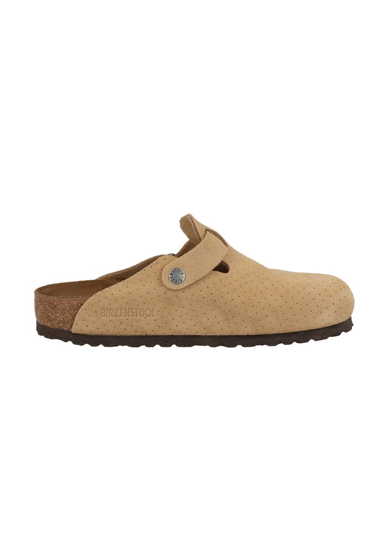 Beige suède klomp met geperforeerde textuur, band met knoopsdetail, kurken middenzool en donkere rubberen loopzool. Merkennaam "BIRKENSTOCK" in reliëf.