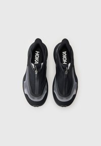Baskets de sport noires avec fermeture éclair, en matériaux en maille et en caoutchouc, au design arrondi et à semelle texturée. Logo de la marque visible sur la semelle intérieure.