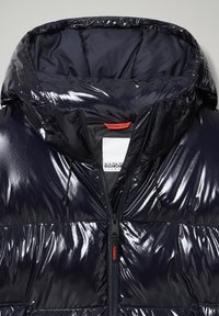 Chaqueta acolchada azul marino con acabado brillante, capucha grande, cremallera frontal y cordones ajustables. Presenta una etiqueta de marca en rojo en el cuello. Superficie texturizada.