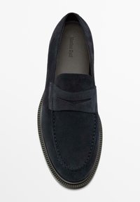 Chaussure à enfiler en daim bleu marine avec un accent rectangulaire, des détails de surpiqûres texturées et une semelle en caoutchouc contrastée. Design minimaliste, bout rond.