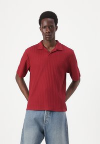 Red ribbed polo shirt with short sleeves and a flat collar, paired with light blue denim jeans. Smooth texture and regular fit design.