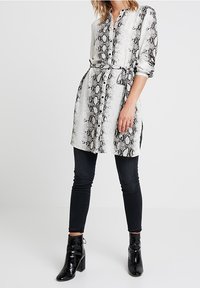 Košilová šaty v černobílé hadí potisku, s límečkem, dlouhými rukávy a páskem v pase. V kombinaci s černými skinny jeans a kotníkovými botami.