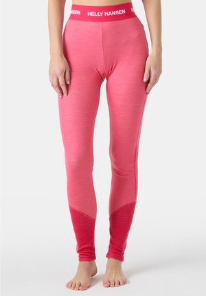 Primer plano de una persona que lleva leggings rosa de Helly Hansen con una pretina con marca, de pie descalza frente a un fondo liso.