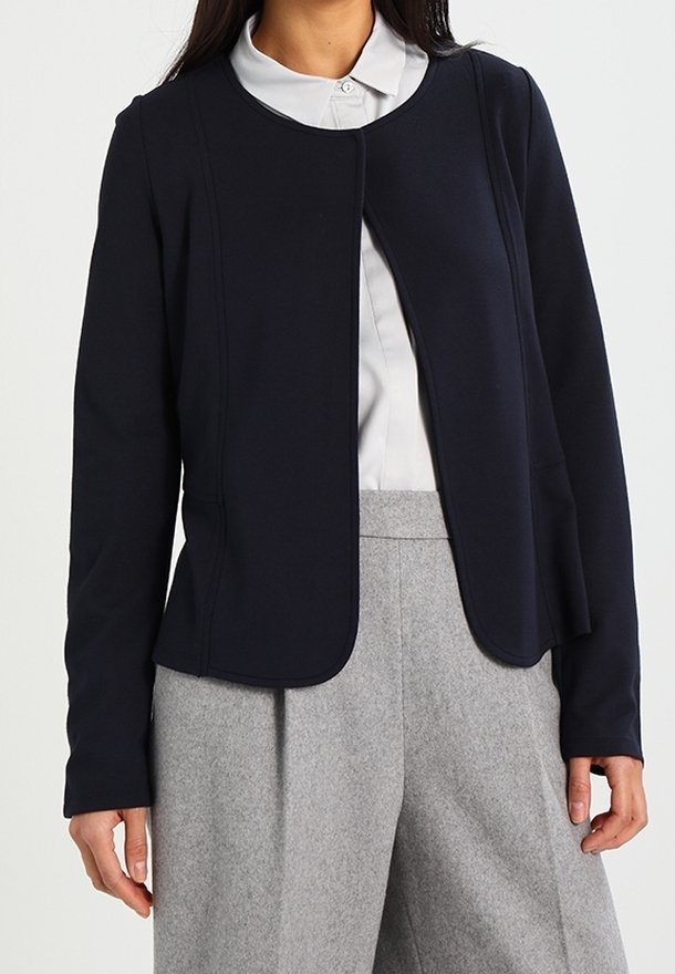 Laivastonsininen takki, joka on valmistettu sileästä kankaasta, pyöreällä pääntiellä, edestä suljettava ja räätälöidyllä istuvuudella, yhdistetty vaaleanharmaisiin housuihin.