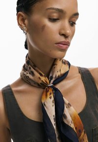 Siidist sall, millel on leopardimuster maapinna toonides pruunis, oranžis ja mustas, seotud korralikult kaela ümber hõbedase sõrmusega aksessuaarina.