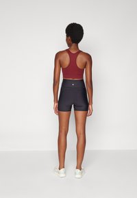 Top sportivo aderente borgogna con design racerback abbinato a pantaloni corti atletici neri a vita alta, caratterizzati da una texture liscia e uno stile minimalista.