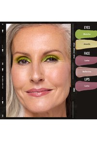 Donna matura con capelli grigi indossa ombretto verde brillante, trucco viso rosa chiaro e labbra lucide rosa, accanto a campioni di colore per il trucco etichettati.