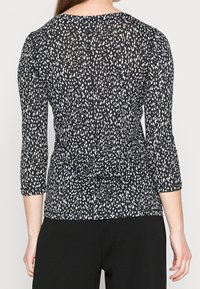 Černobílý vzorovaný top s tříčtvrtečními rukávy, volného střihu a uzlem na zadní straně. Vyrobeno z lehkého materiálu.