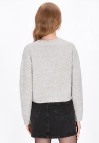 Hellgrauer, gestrickter Pullover mit einem verkürzten Design und langen Ärmeln, kombiniert mit einem schwarzen Jeans-Minirock. Weicher Stoff und gerippte Details.