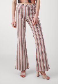 Personne portant un pantalon évasé taille haute à rayures verticales rouges, marine et beige, associé à des talons blocs ouverts couleur nude.