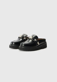 Black leather slip-on shoes with a chunky sole, featuring decorative silver hardware and stitching accents along the edges.