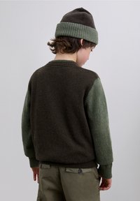 Kaksivärinen villapaita, jossa tummanruskea vartalo ja vihreät hihat. Varustettu resorireunuksilla hihansuissa ja kauluksessa. Yhdistetty khakinvärisiin cargo-housuihin.